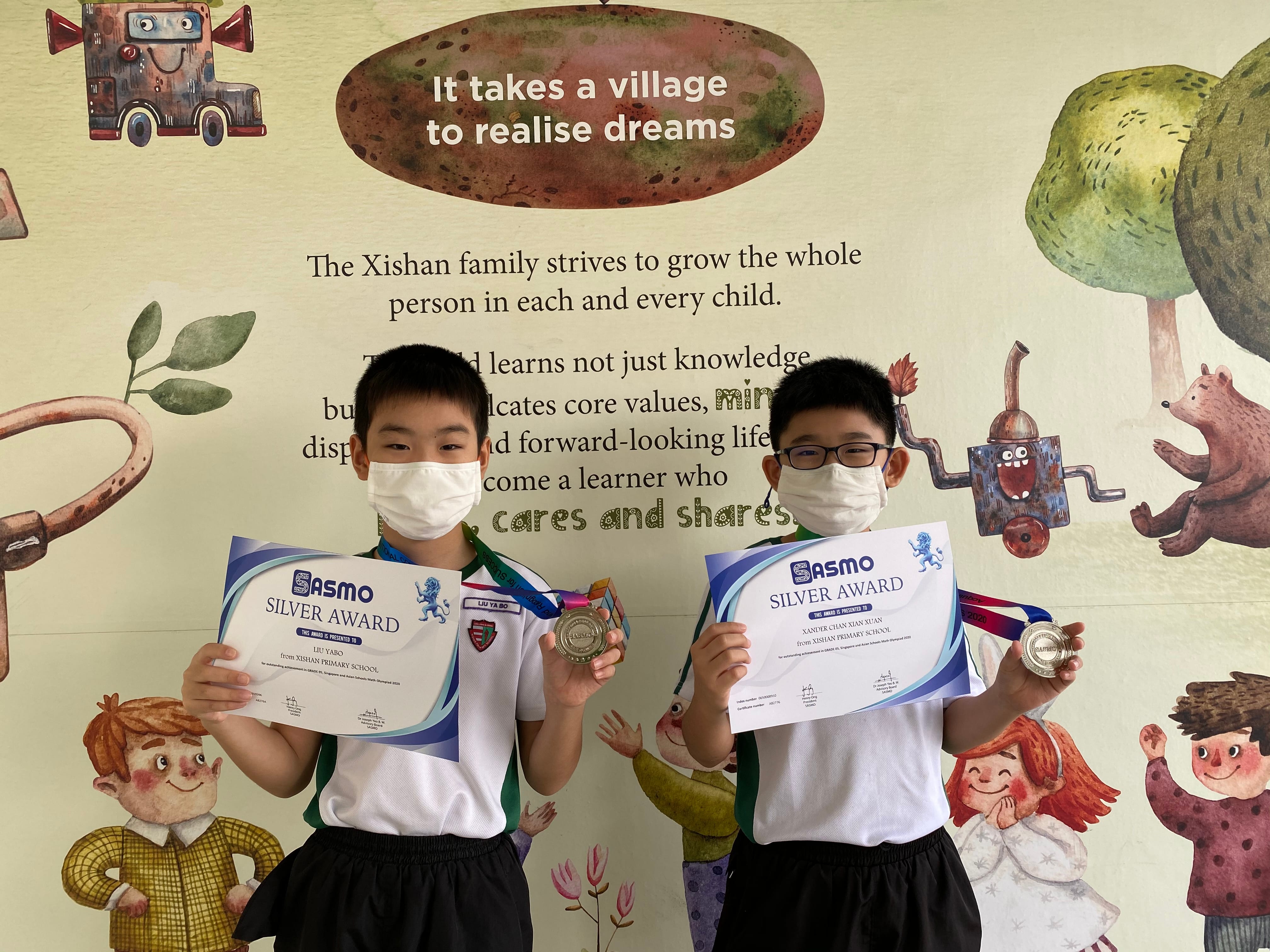 Two masked boys hold SASMO Silver Award certificates and medals in front of a Xishan Primary School mural.